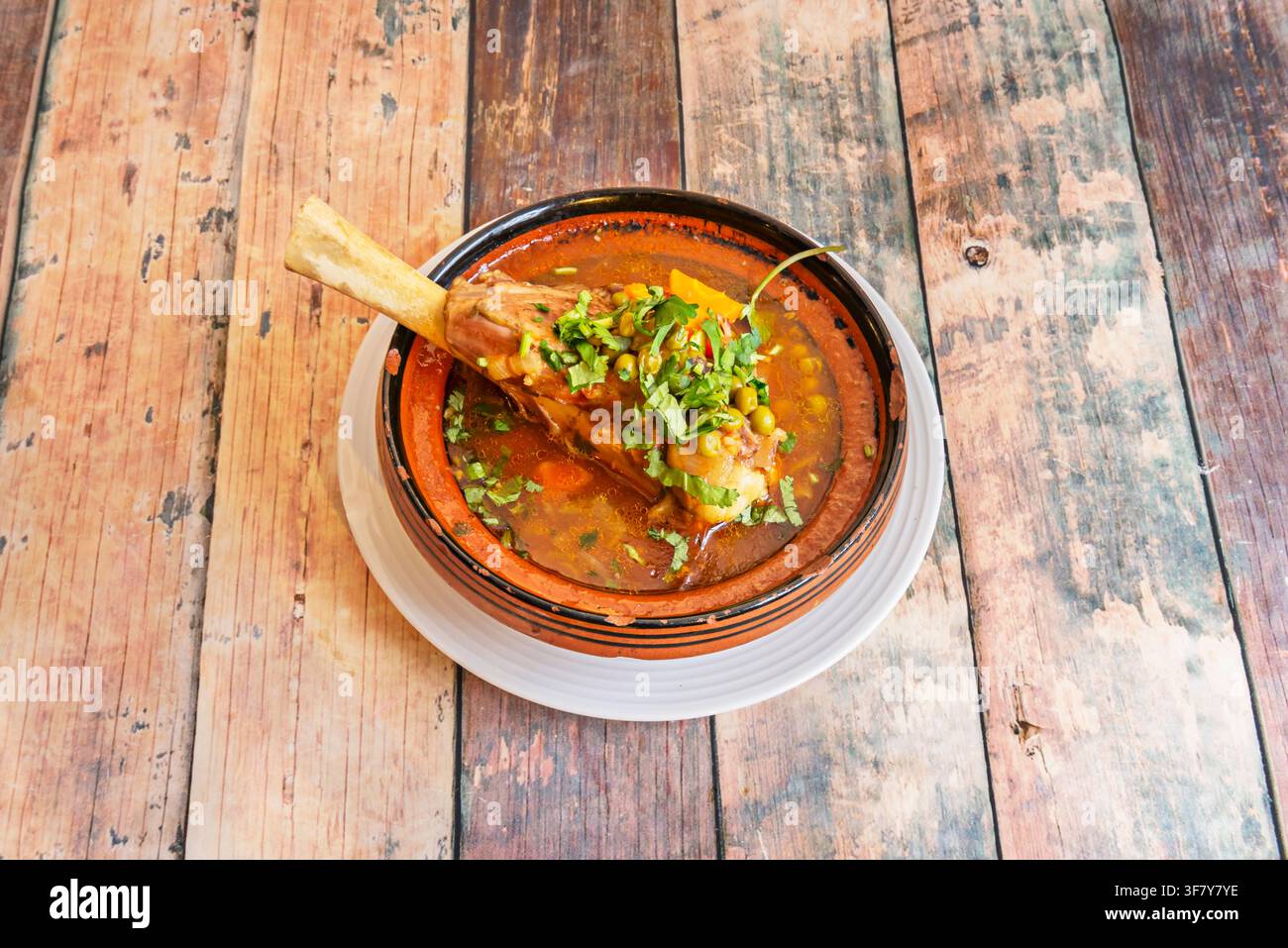 Stinco d'agnello brasato con piselli, carote e coriandolo, servito in una ciotola tradizionale in argilla (tagine) Foto Stock