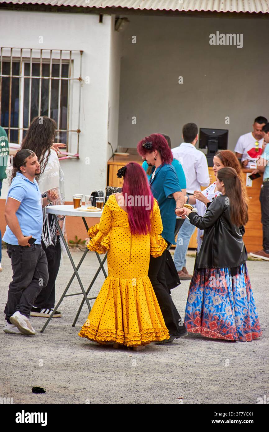 I visitatori del festival si radunano intorno a tavoli in piedi, tra cui una donna in un abito stile flamenco a pois giallo brillante con maniche e gonna a balze, d Foto Stock