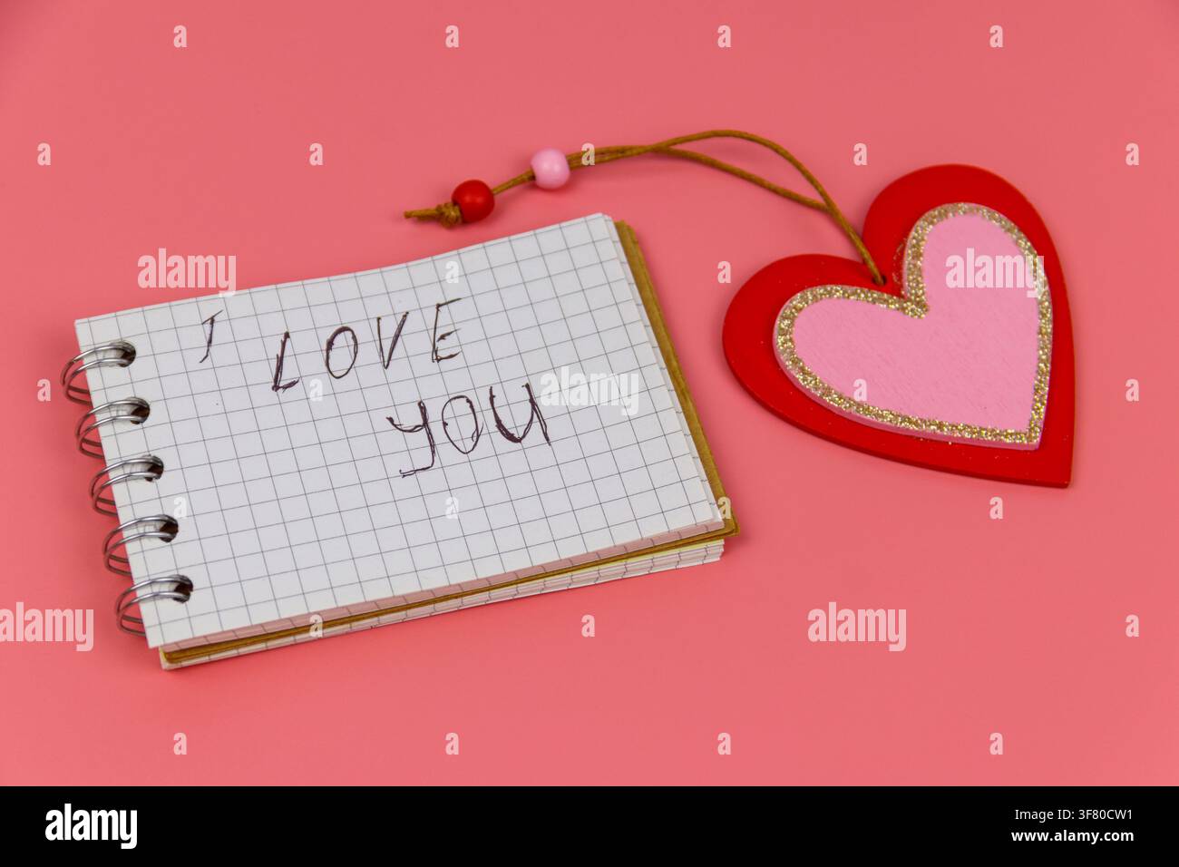 Cuore e blocco note con testo scritto a mano "Ti amo" su sfondo rosa pastello. Concetto di San Valentino Foto Stock