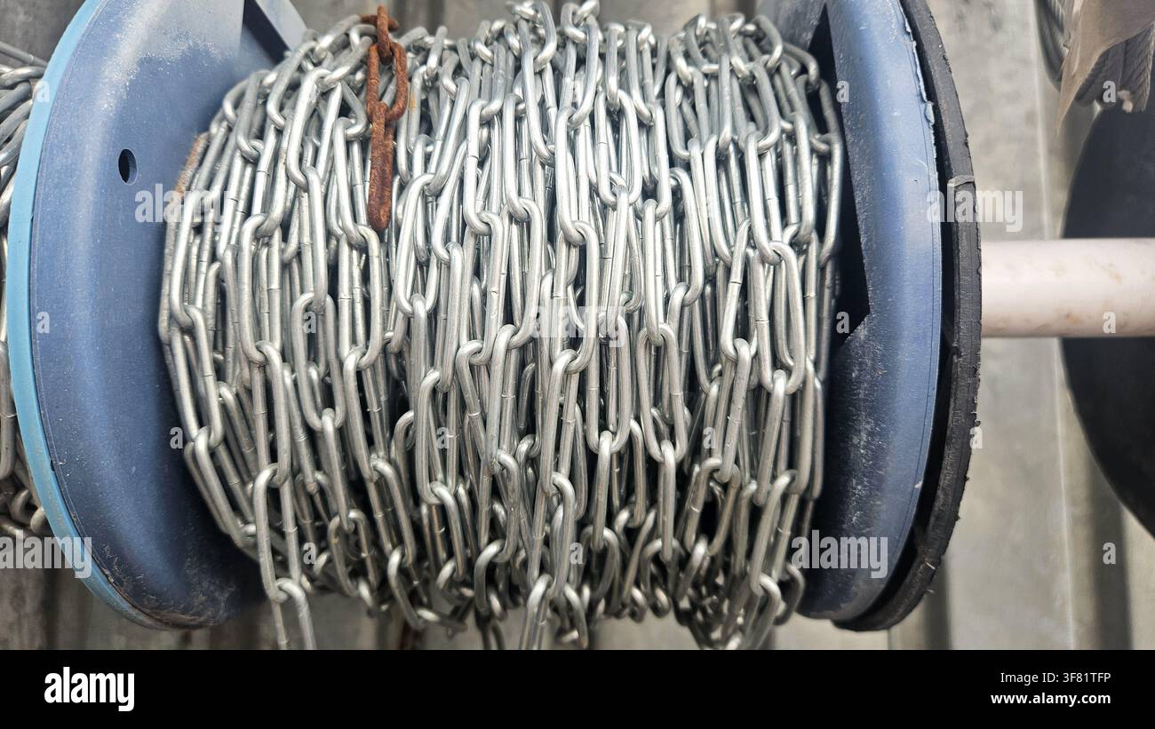 Primo piano di una catena metallica strettamente avvolta su una bobina di plastica blu, perfetta per riferimenti di attrezzature industriali, visuali di costruzione e applicazioni pesanti Foto Stock