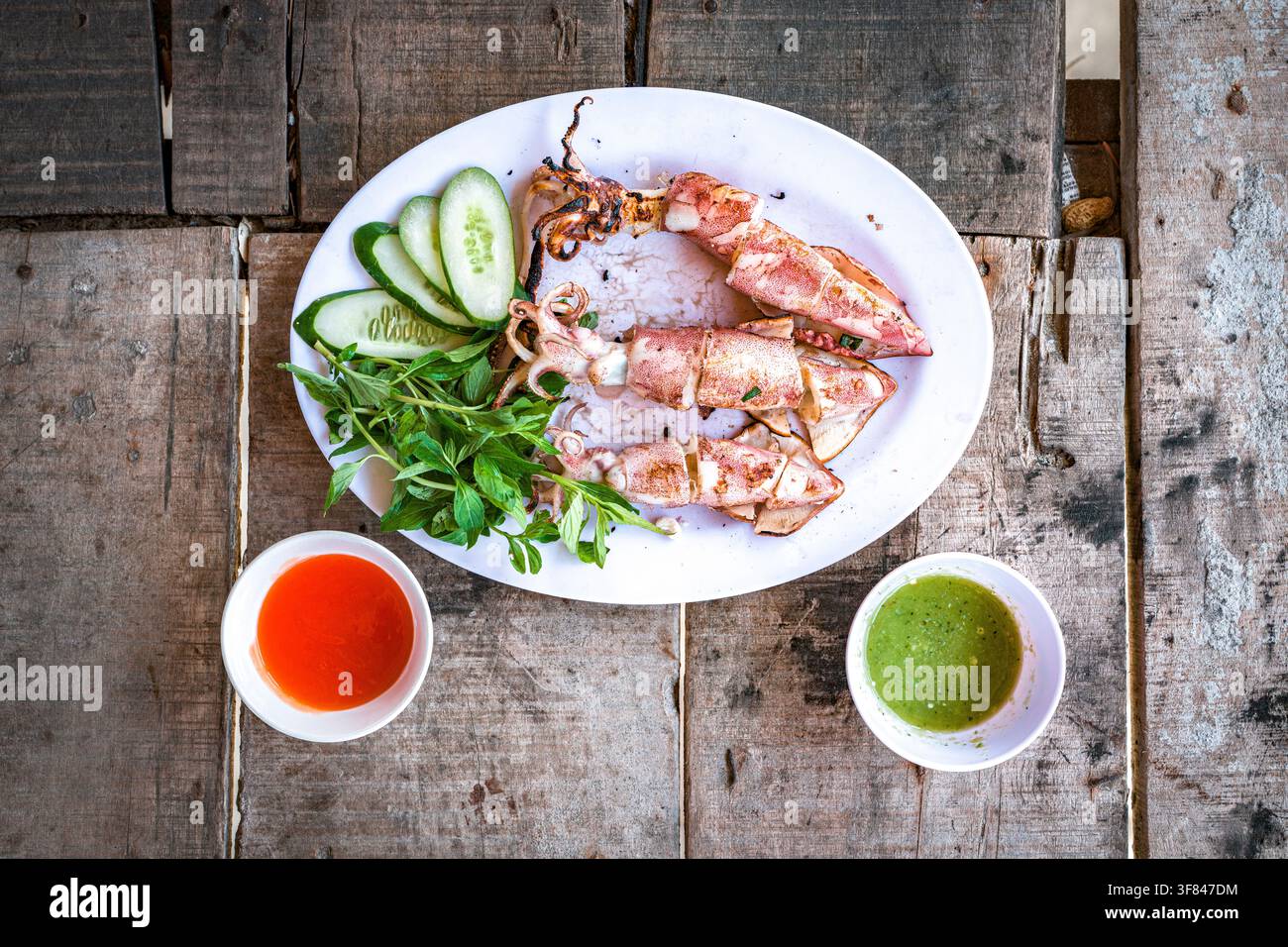 Calamari grigliato servito con erbe e salse su un tavolo di legno in Vietnam per un'esperienza culinaria tradizionale Foto Stock