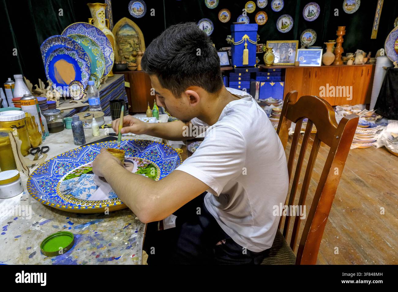 Giovane artigiano dipinge un piatto in una bottega a Samarcanda, Uzbekistan Foto Stock