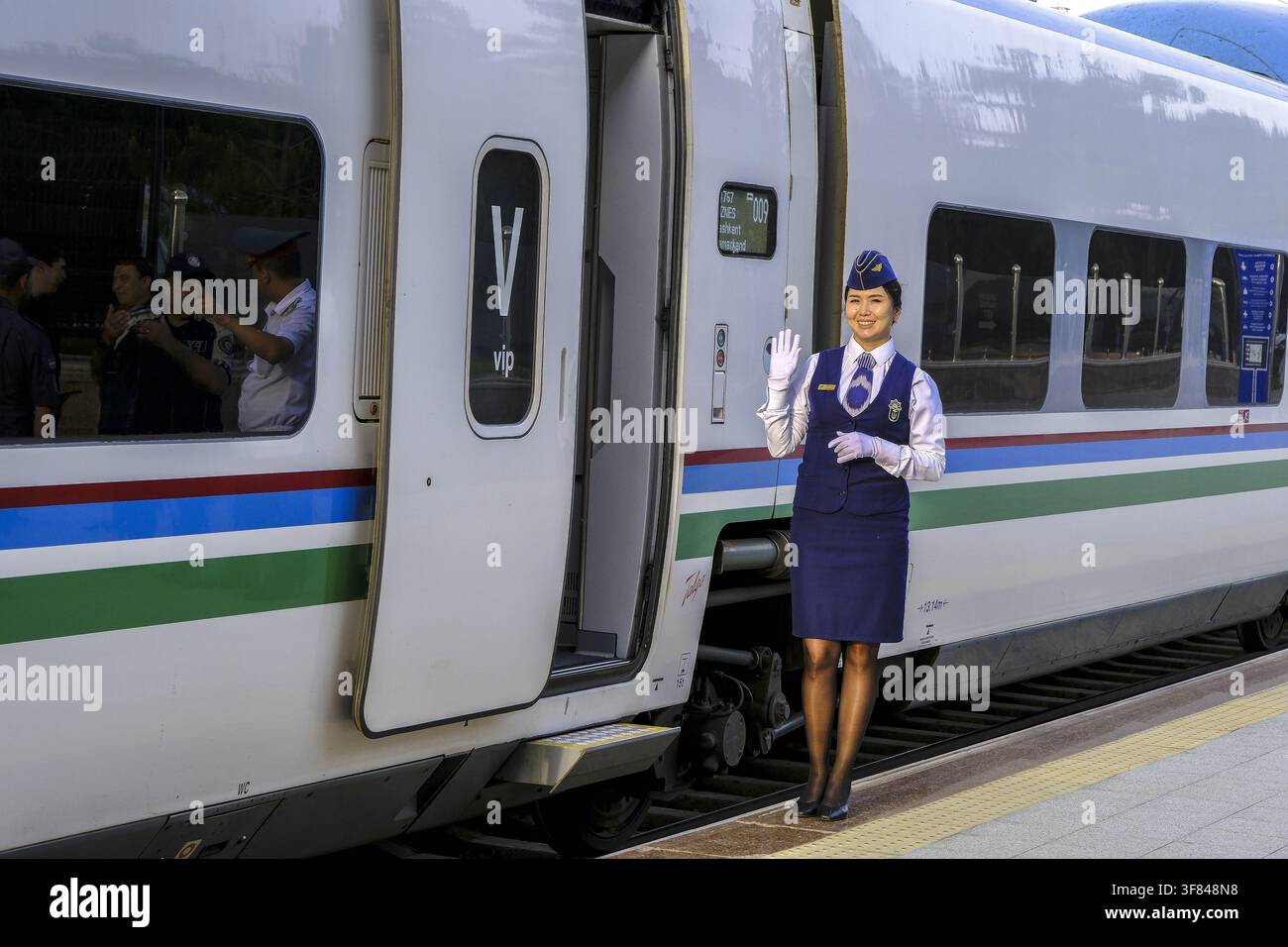 Treno veloce alla stazione di Samarcanda con un membro del personale che accoglie i passeggeri sul binario Foto Stock