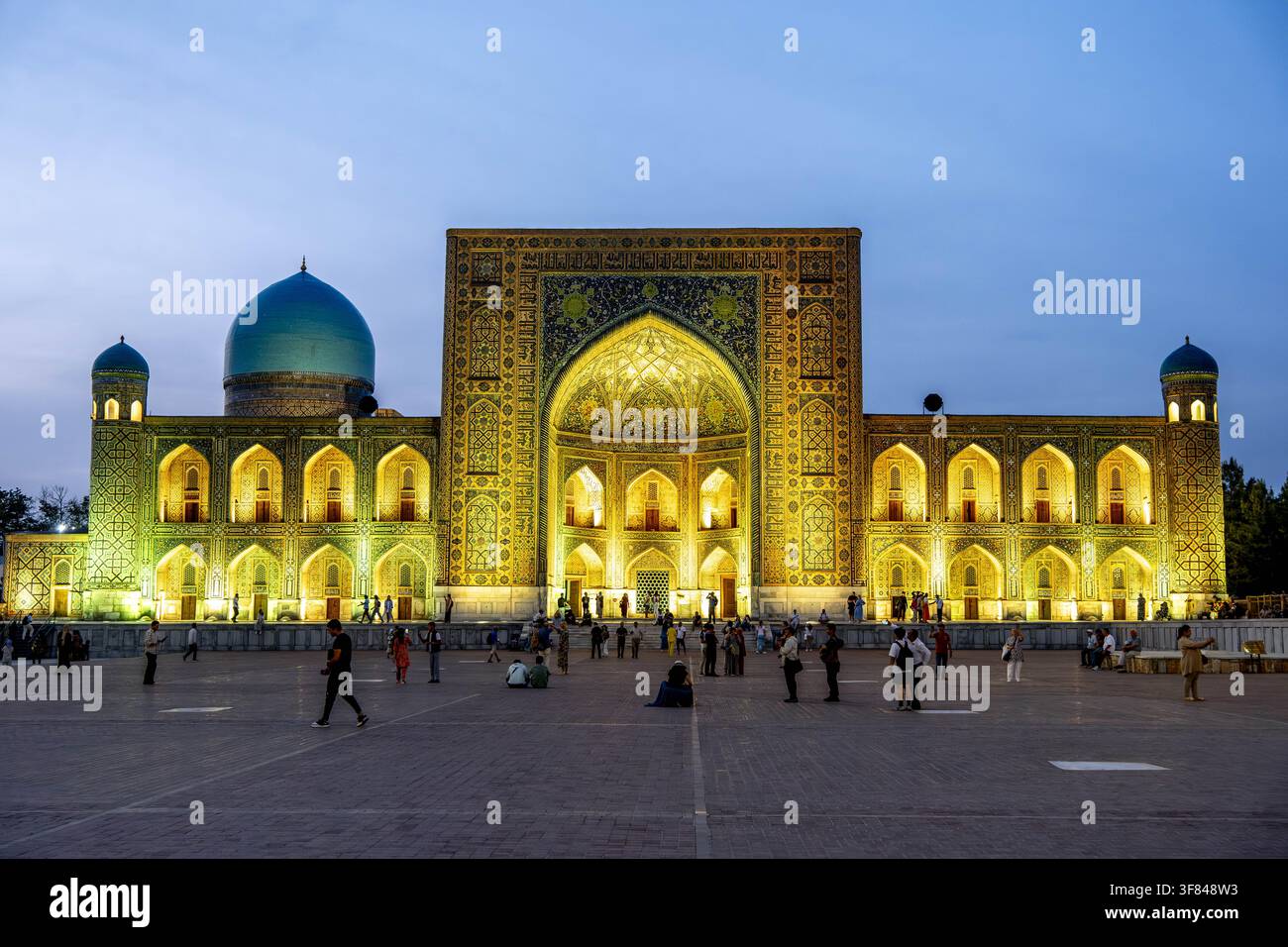 Vista serale del Registan con piazza affollata e luci colorate a Samarcanda, Uzbekistan Foto Stock