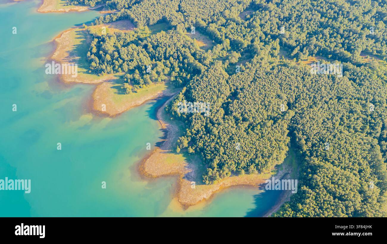 Vista aerea dall'alto dell'acqua turchese brillante del lago Plastiras che incontra una fitta foresta verde lungo una costa frastagliata in Grecia Foto Stock