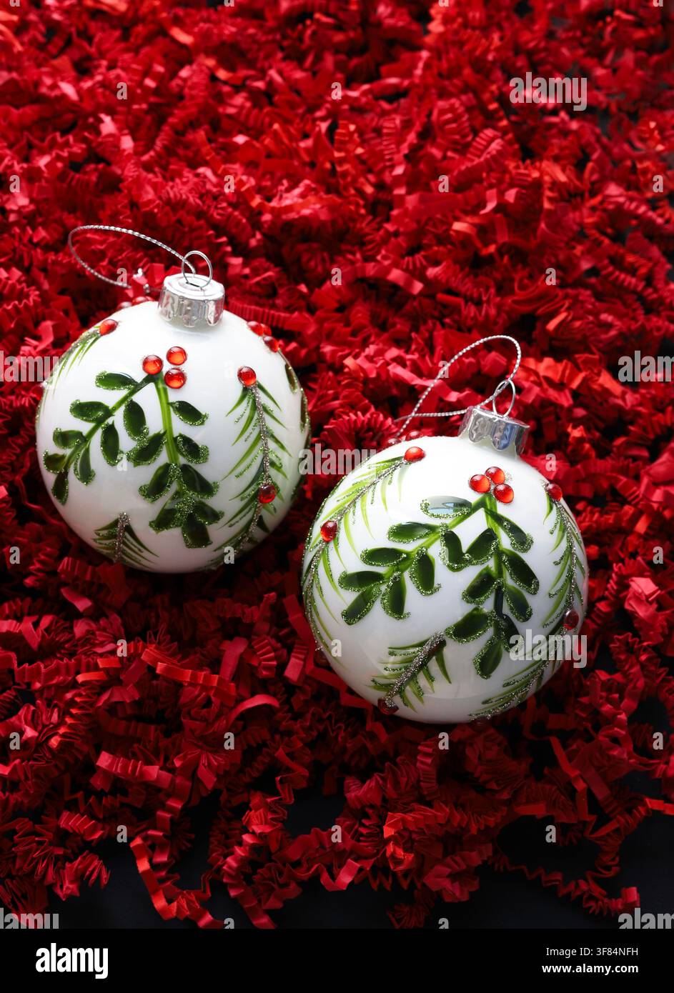 Due palline di Natale in vetro bianco con vischio verde su sfondo rosso, simboleggianti lo spirito natalizio. Stagione natalizia e delle feste. Foto Stock