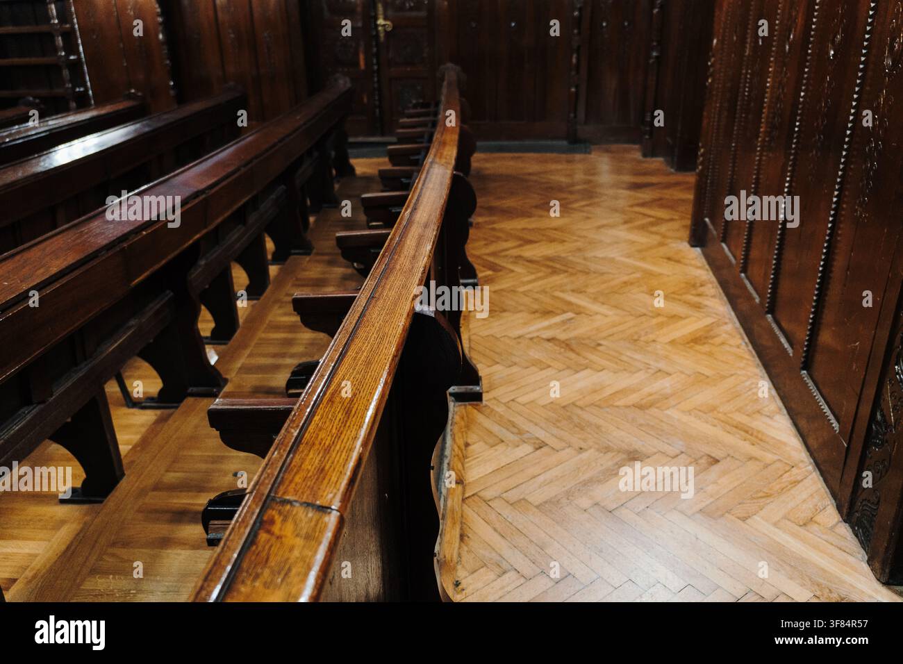 Lunghi filetti di panche in legno lucido all'interno di un interno storico tradizionale. Architettura classica con lavori di intaglio del legno artigianali e pavimenti in parquet. Foto Stock