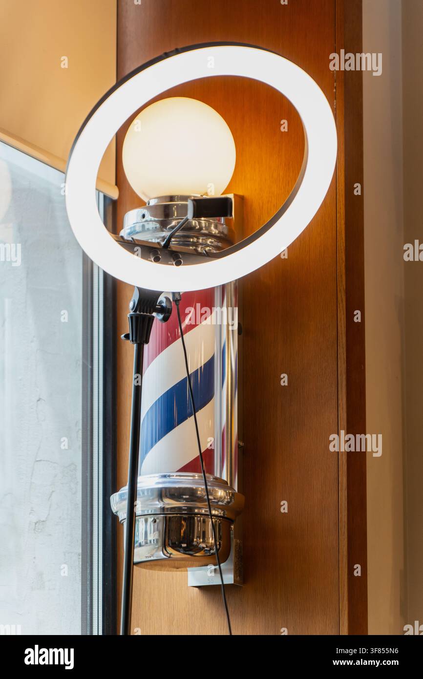 Classico palo da barbiere rosso bianco e blu circondato da una luce LED circolare moderna, che rappresenta l'innovazione del servizio, il branding personale e lo stile estetico Foto Stock