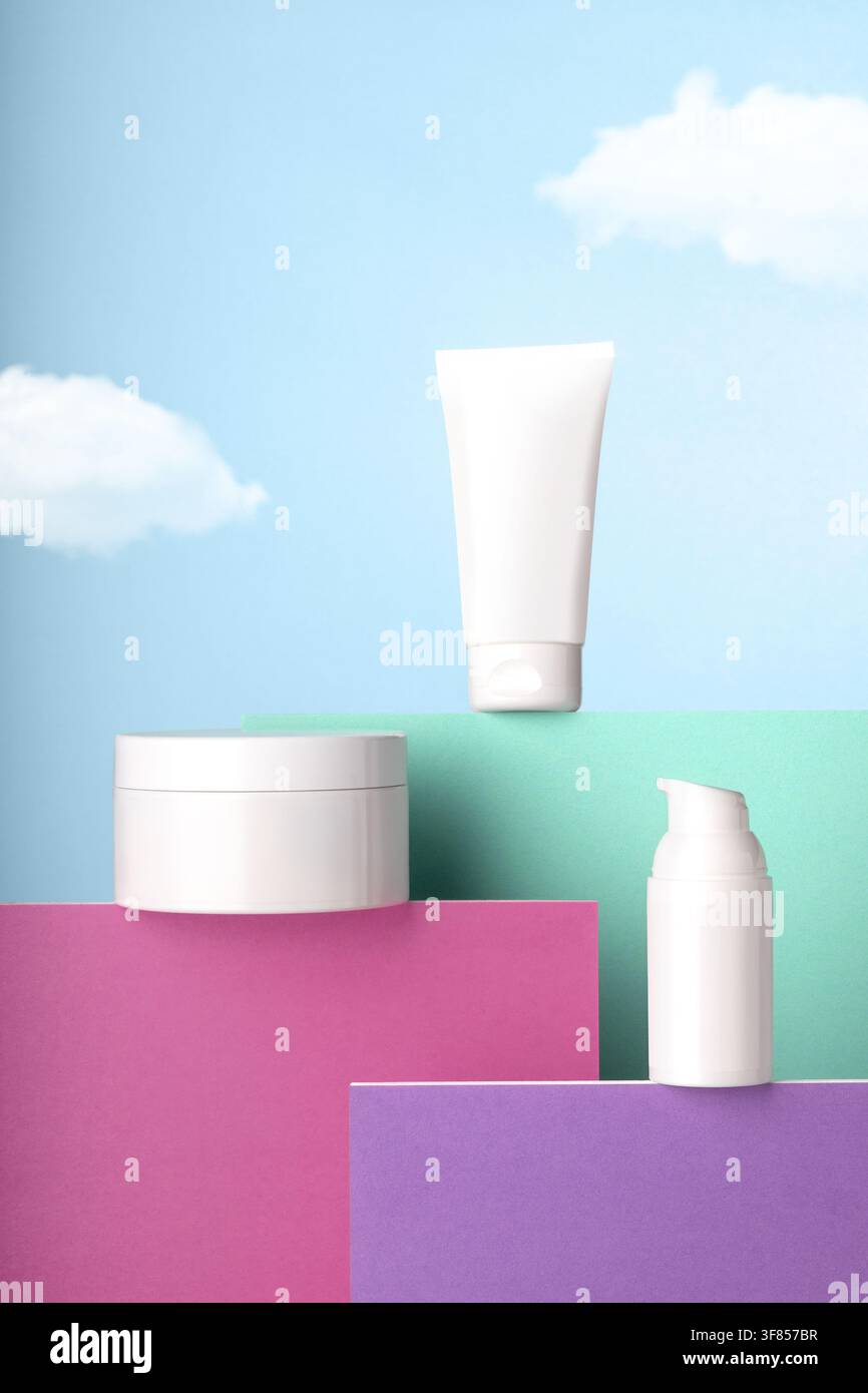 Prodotti per la cura della pelle cosmetica bianchi vuoti su piedistalli colorati con sfondo di cielo blu. Foto Stock