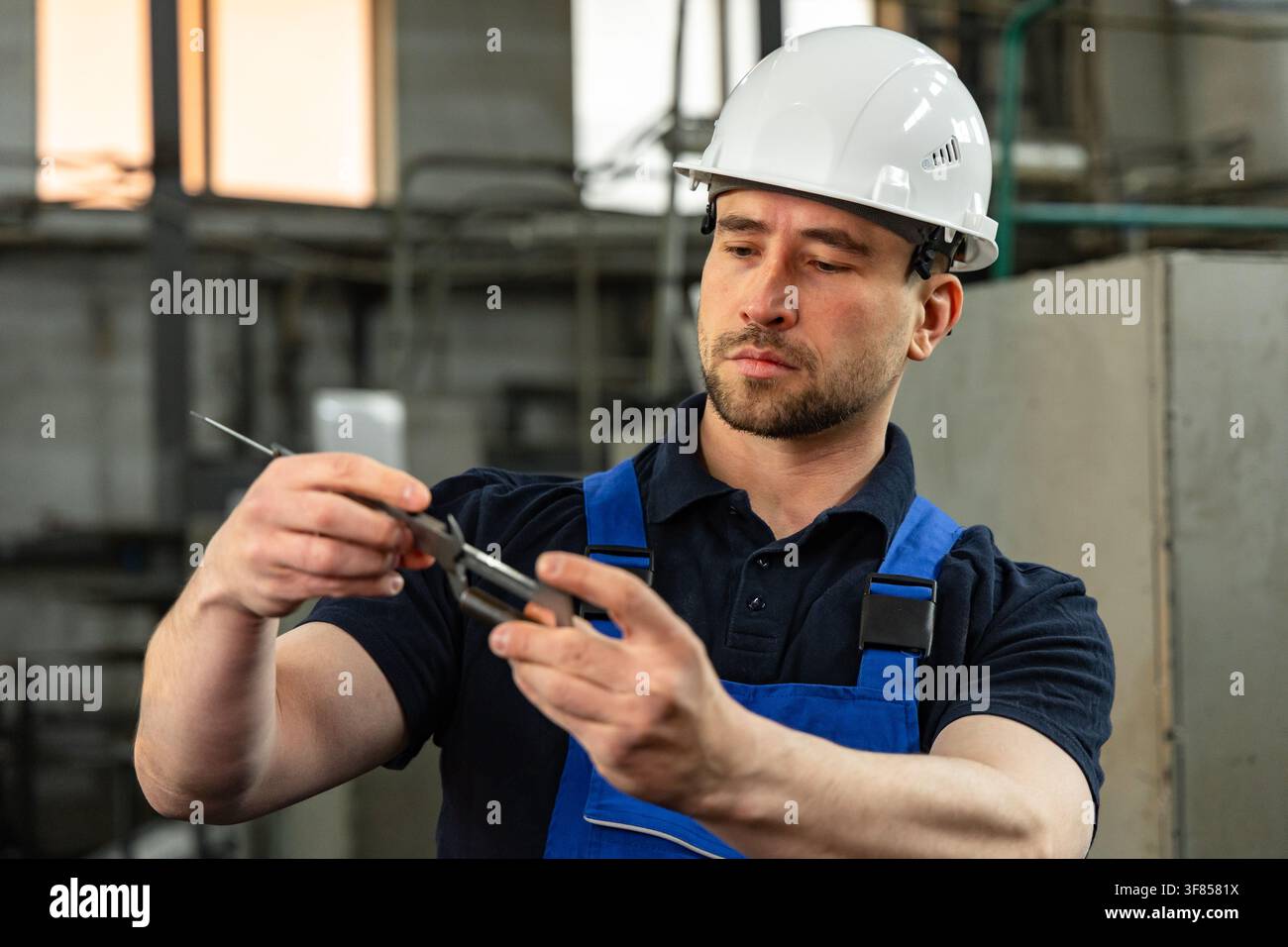 Operaio di fabbrica che misura un componente metallico con un calibro di precisione Foto Stock
