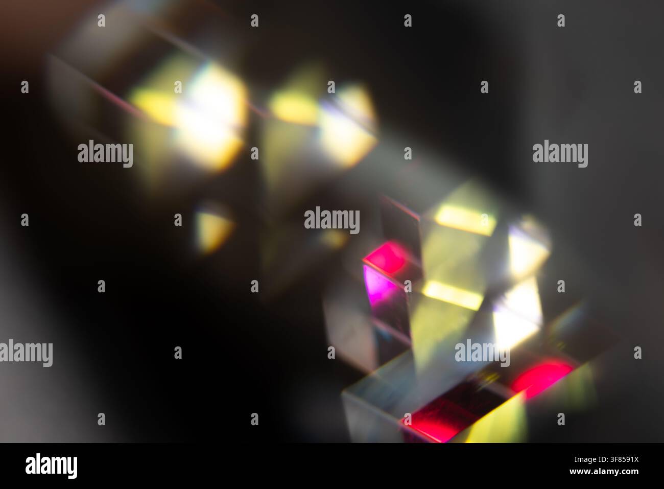 Prismi di vetro che rifrangono luce gialla brillante, rosa e bianca su uno sfondo scuro per un design ottico astratto Foto Stock