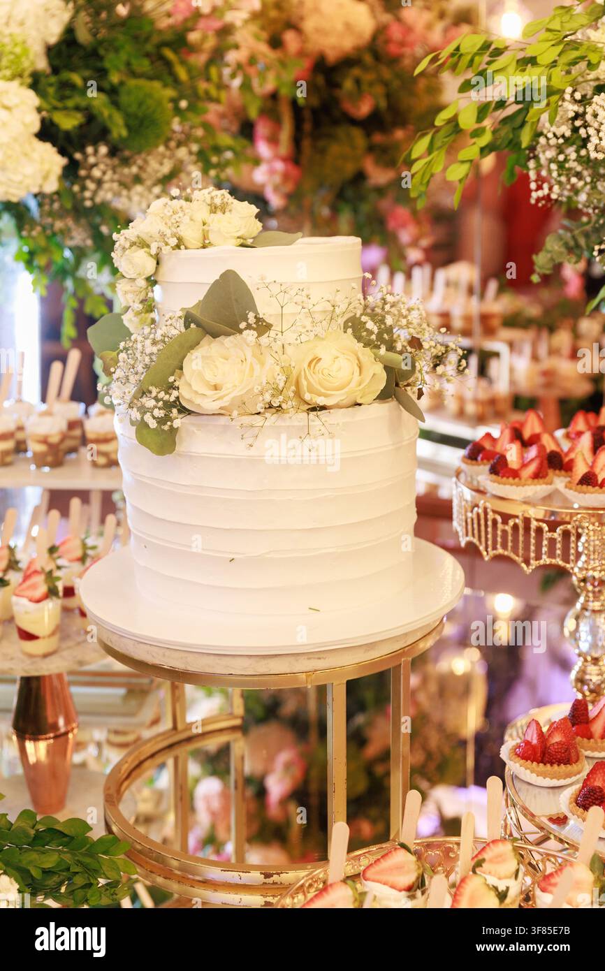 Prima vista di una torta nuziale a due piani decorata con fiori freschi su un elegante tavolo da dessert per la reception durante la celebrazione del matrimonio Foto Stock
