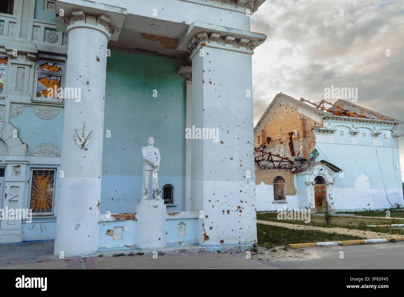 Edificio del patrimonio danneggiato con segni di schegge sulle colonne bianche e statua in piedi dopo un bombardamento militare durante un conflitto armato Foto Stock