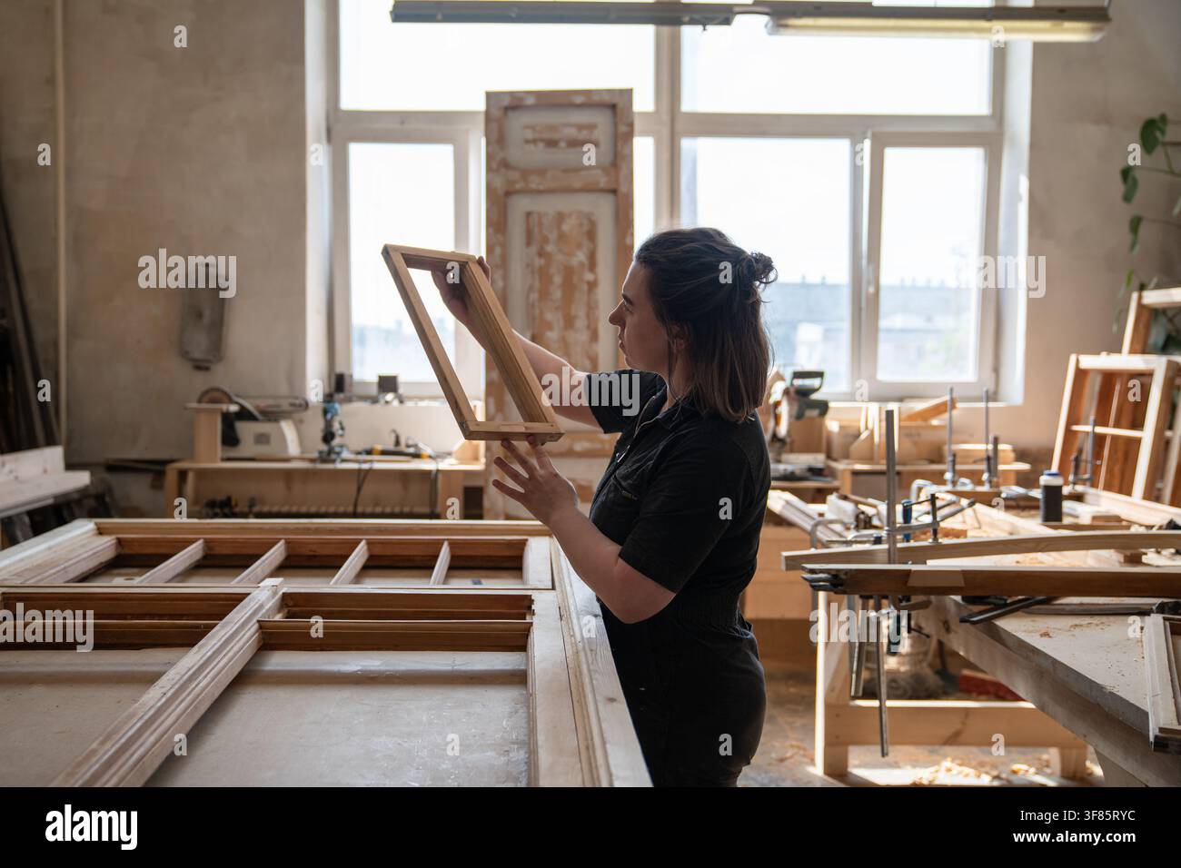 Falegnama tiene in mano una parte di una cornice di finestra antica esaminando la qualità del pezzo di legno. Foto Stock