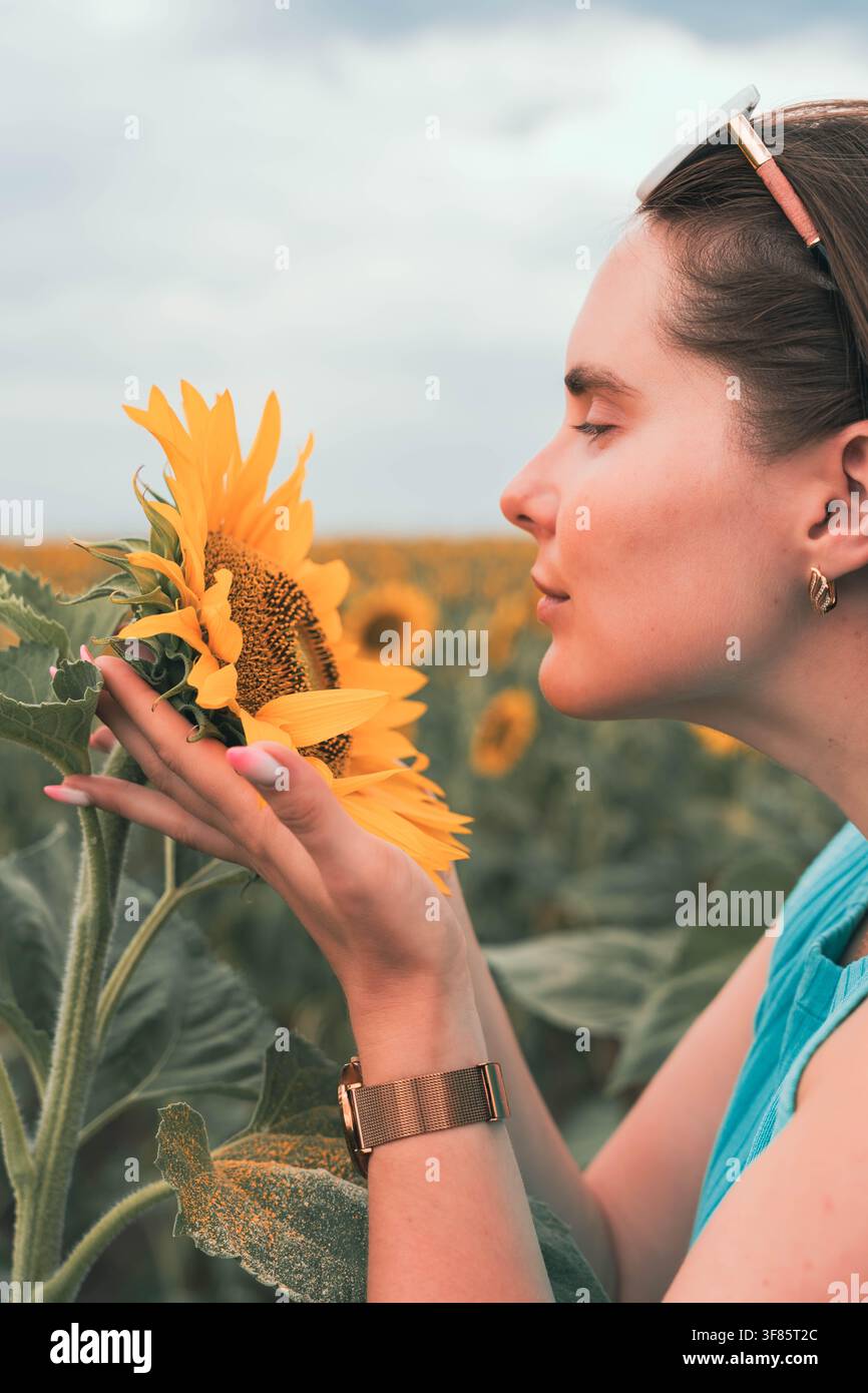 Donna che tiene un girasole, in un campo di girasoli, con girasole, orologio, da una prospettiva di profilo laterale, con accenti gialli e blu, e un'atmosfera serena Foto Stock