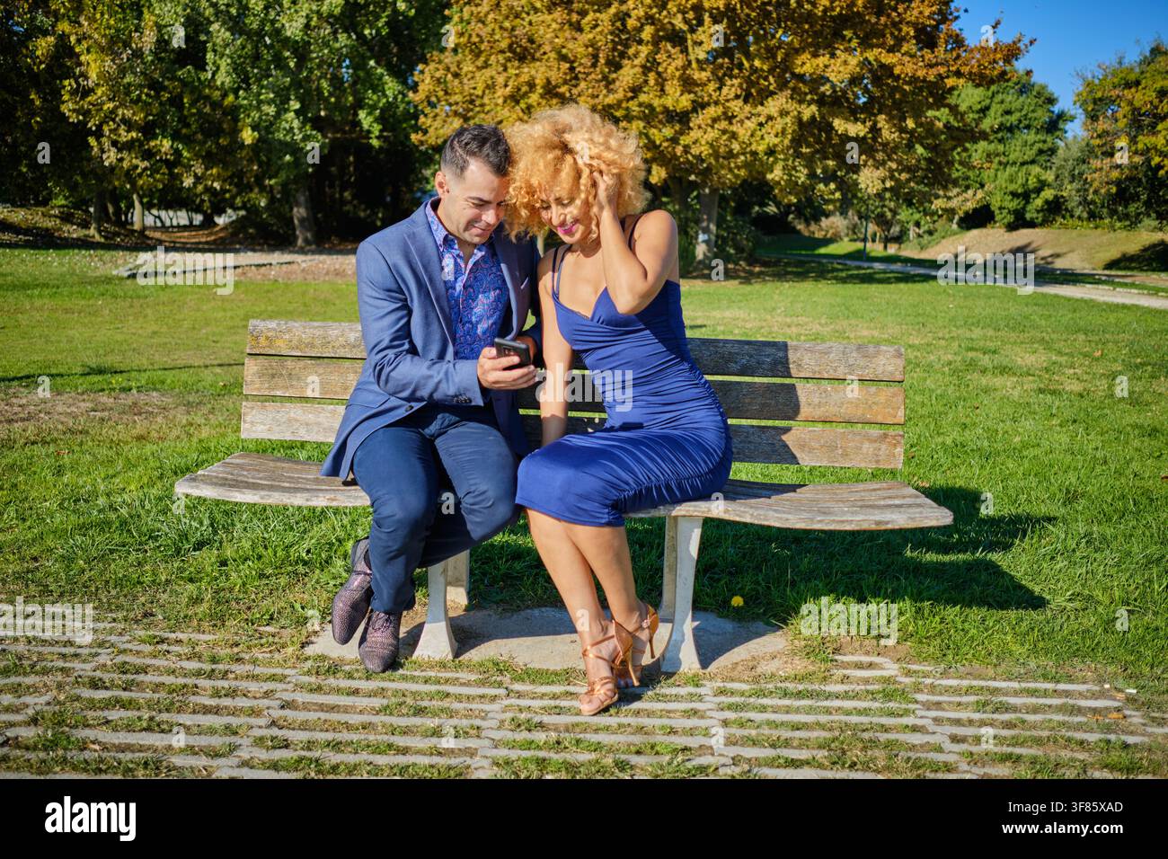 Coppia sorridente che condivide uno smartphone su una panchina del parco all'aperto Foto Stock