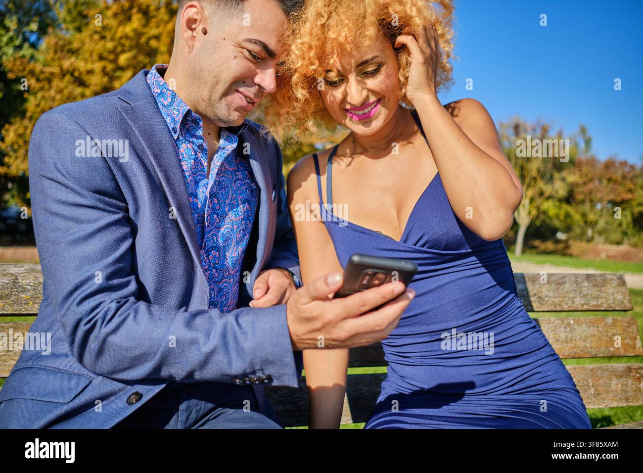 Giovane coppia che godersi i contenuti digitali ridendo insieme su una panchina del parco all'aperto Foto Stock