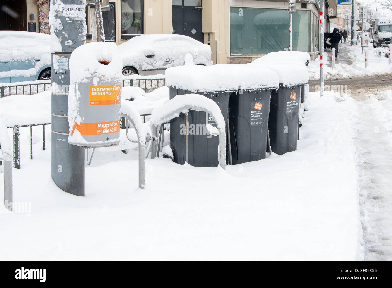 VIENA, AUSTRIA, 20 FEBBRAIO 2026: Diversi contenitori per rifiuti e un bidone pubblico sono pesantemente coperti di neve lungo un marciapiede cittadino dopo la nevicata Foto Stock