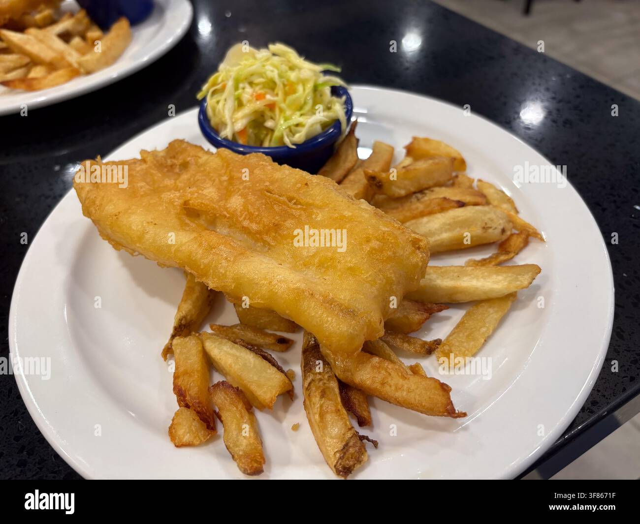 Pesce fritto e patatine fritte serviti su un piatto bianco con insalata di cavolo. Foto Stock