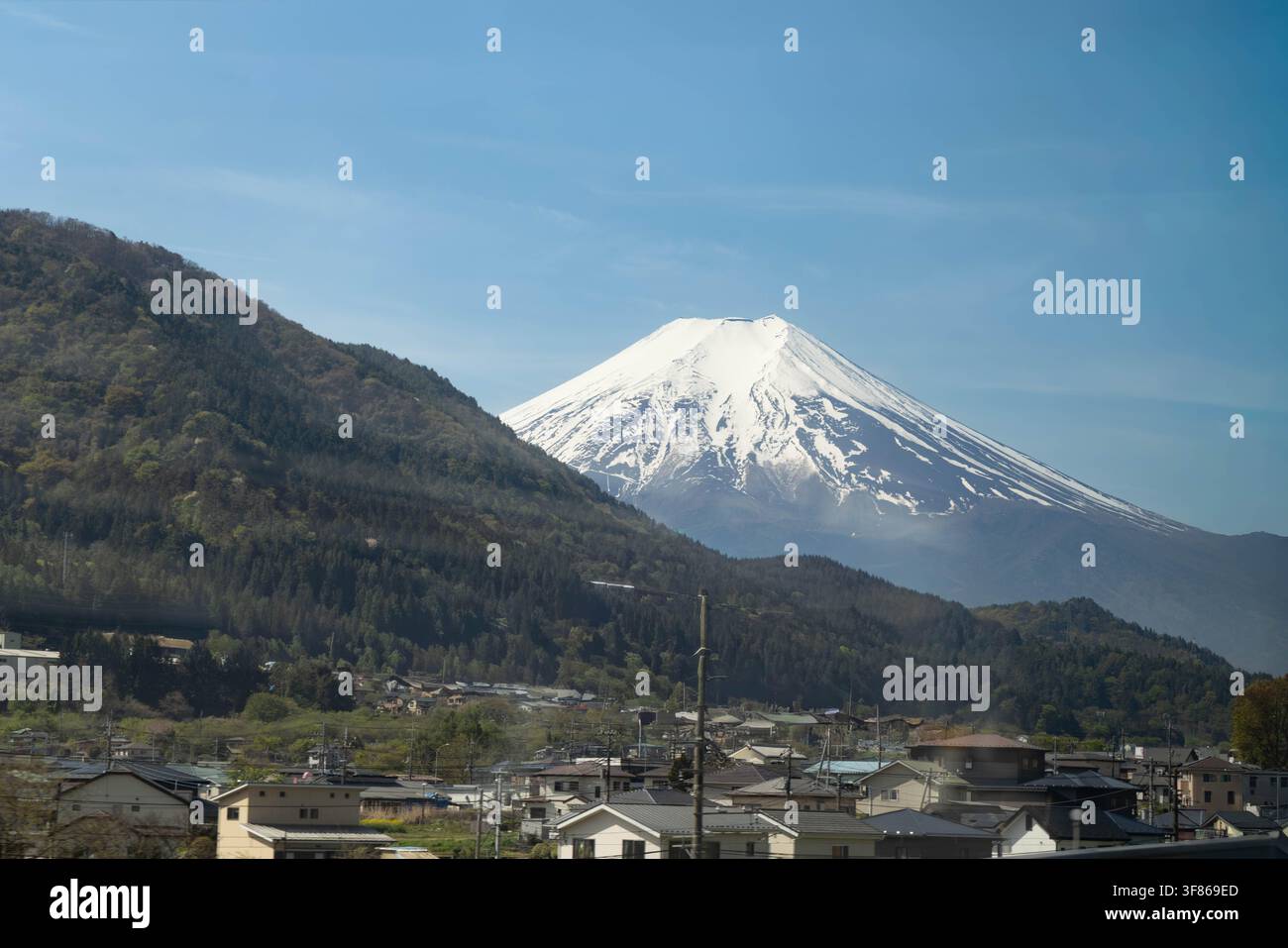 La cima innevata del vulcano Monte Fuji tra l'area alberata e un piccolo villaggio con case Foto Stock