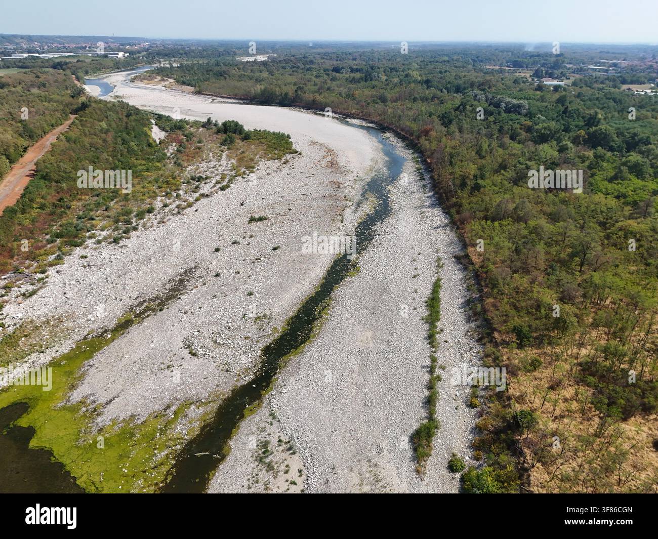 Vista aerea del fiume Sesia con un livello dell'acqua notevolmente ridotto e un letto roccioso esposto a causa di una grave siccità, circondato da una vegetazione lussureggiante Foto Stock