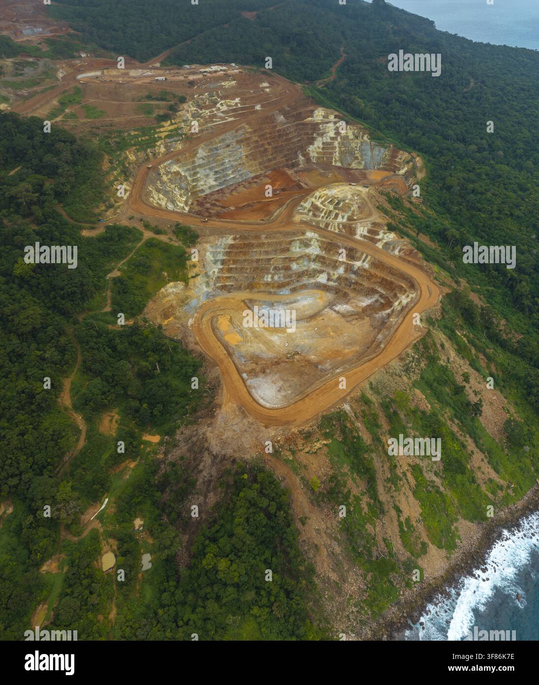 Vista aerea della miniera d'oro e rame di Tujuh Bukit che mostra fosse di scavo a terrazze, strade sterrate sinuose e la fitta foresta tropicale circostante a Kec Foto Stock