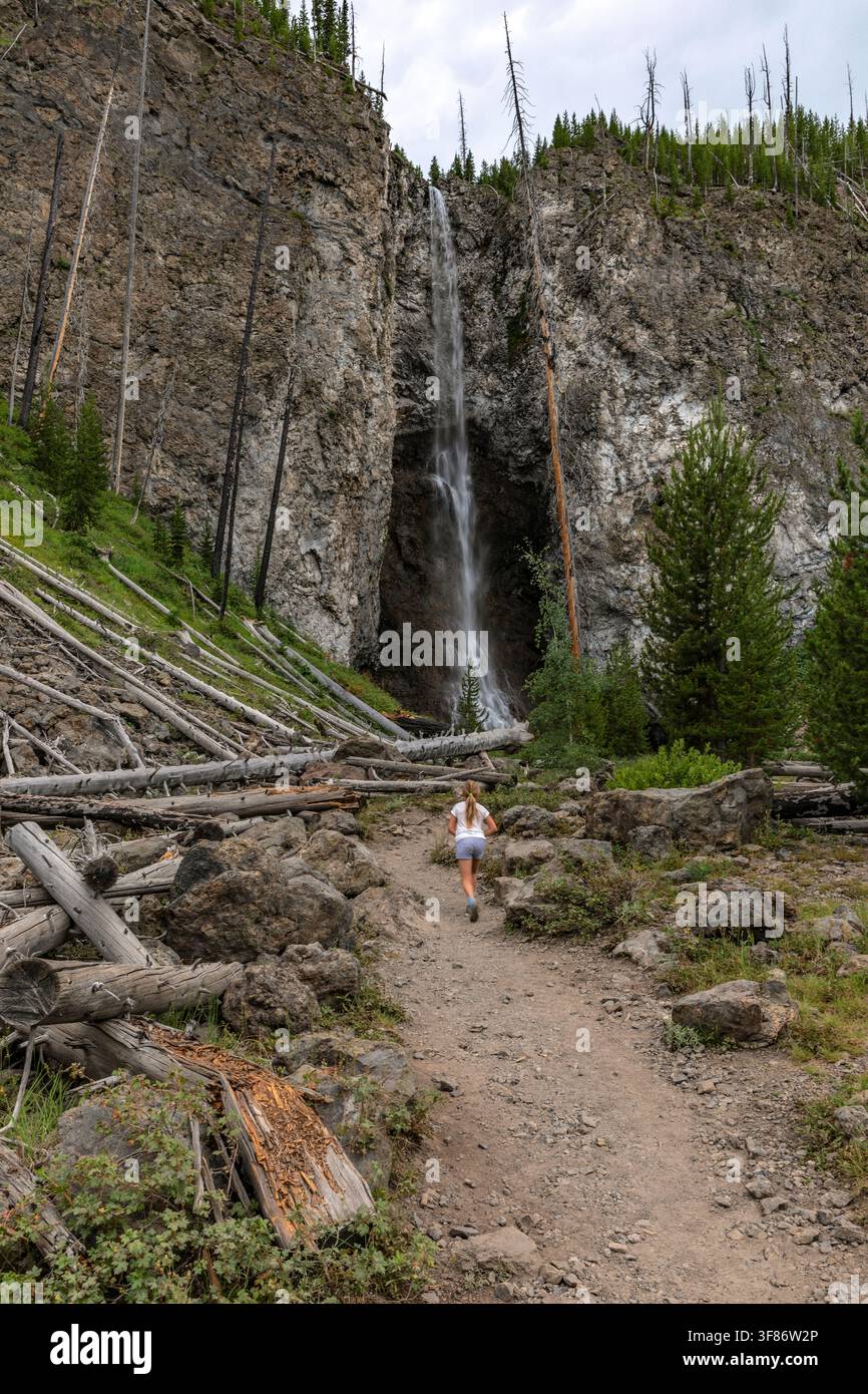 Escursionista donna percorre un sentiero sterrato verso Fairy Falls, una cascata di 200 piedi nel parco nazionale di Yellowstone, Wyoming, oltre alberi bruciati e tronchi caduti Foto Stock