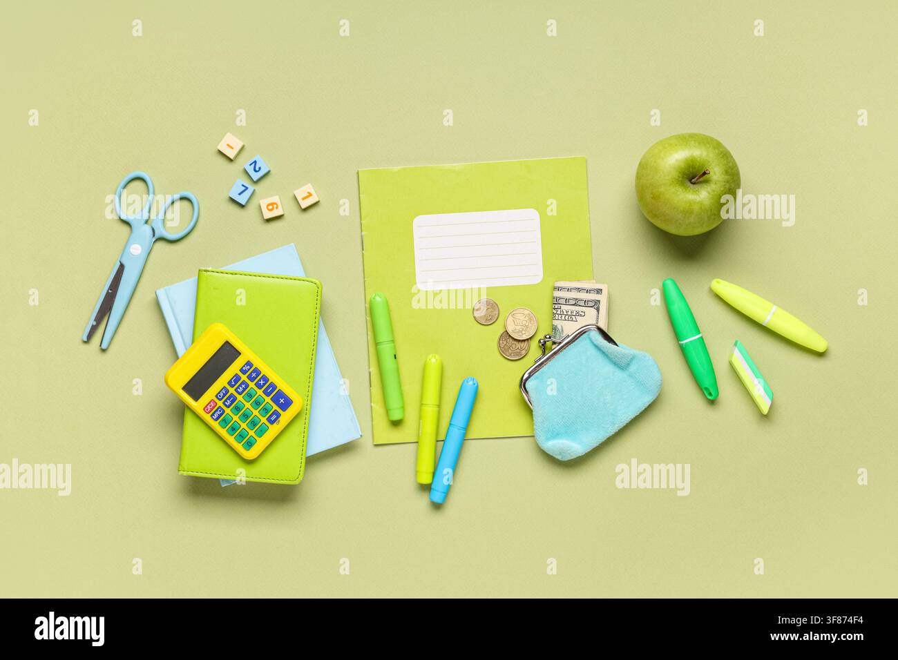 Materiali scolastici e alfabetizzazione finanziaria con calcolatrice, denaro e mela su uno sfondo verde Foto Stock