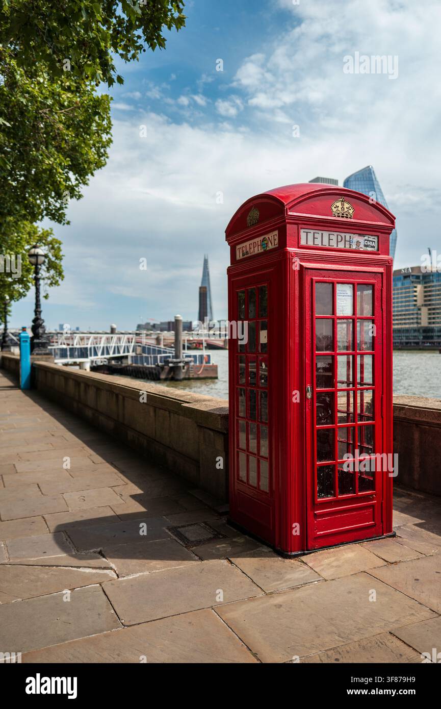 Cabina telefonica rossa tradizionale accanto al Tamigi a Londra, con edifici moderni della città sullo sfondo. Foto Stock