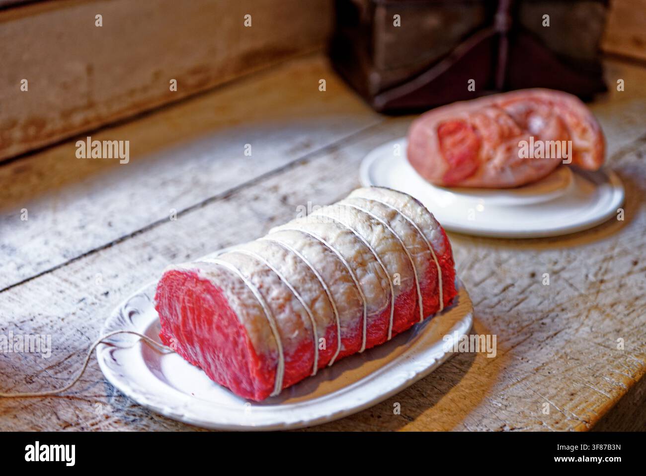 Un bel taglio di carne cruda arrotolato e legato con spago da macellaio, accanto a salsicce su piatti di ceramica a Lanhydrock House in Cornovaglia, fotografo Foto Stock