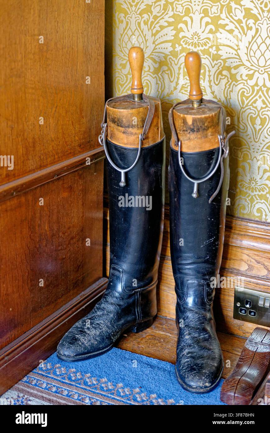 Un paio di stivali da equitazione in pelle nera vintage montati su forme in legno e con speroni in metallo, posizionati in una stanza decorata Foto Stock