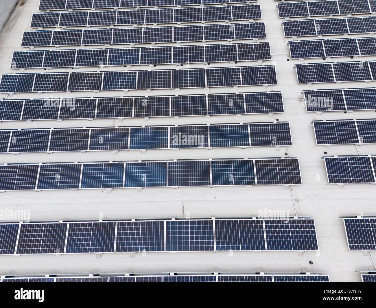 Vista aerea ravvicinata di un grande array di pannelli solari disposti in file diagonali su un tetto piatto commerciale, infrastruttura di energia rinnovabile e fotovoltaico Foto Stock