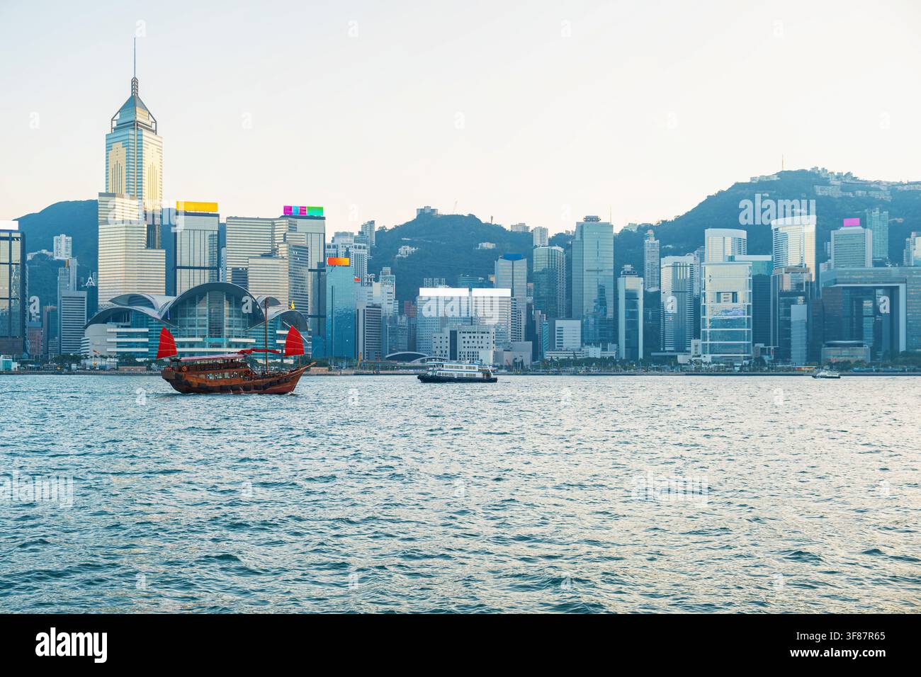 Barca a vela tradizionale sul Victoria Harbour davanti allo skyline moderno della città di Hong Kong, Cina. Architettura contemporanea, turismo, patrimonio culturale Foto Stock