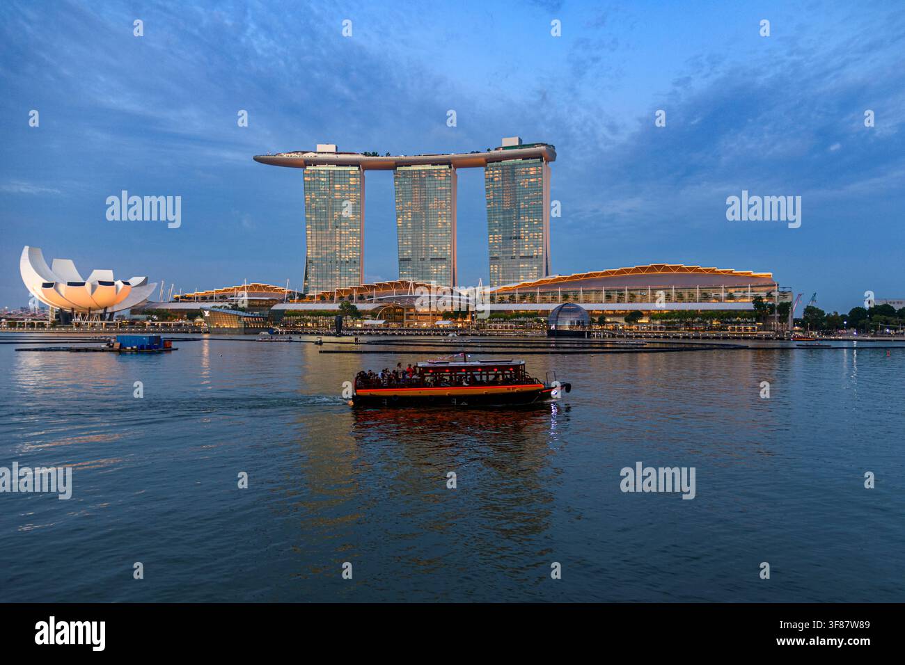 Un Bumboat naviga davanti al Marina Bay Sands Hotel e al Museo ArtScience alla sera, Marina Bay, Singapore Foto Stock