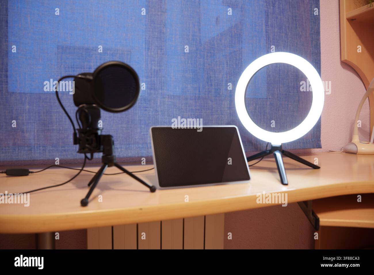 Tablet, microfono e anello luminoso su scrivania di legno accanto a una finestra luminosa, creando un impianto di studio domestico pulito per registrazioni, streaming, insegnamento e digitale Foto Stock