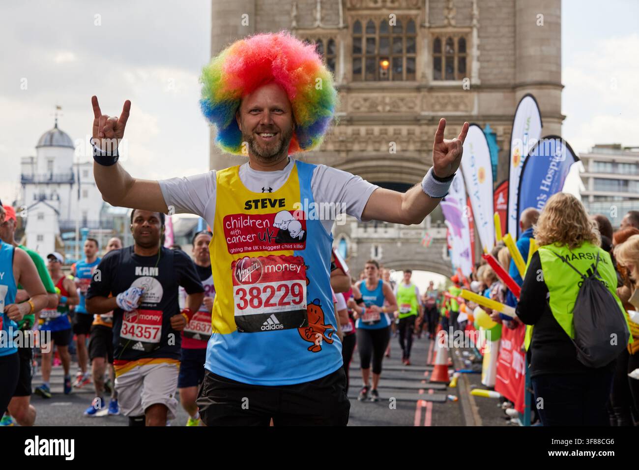 Corridore di beneficenza con parrucca arcobaleno alza entrambe le mani durante il London Marathon durante il London Marathon del 2017 sul Tower Bridge a Londra, Inghilterra, Regno Unito Foto Stock