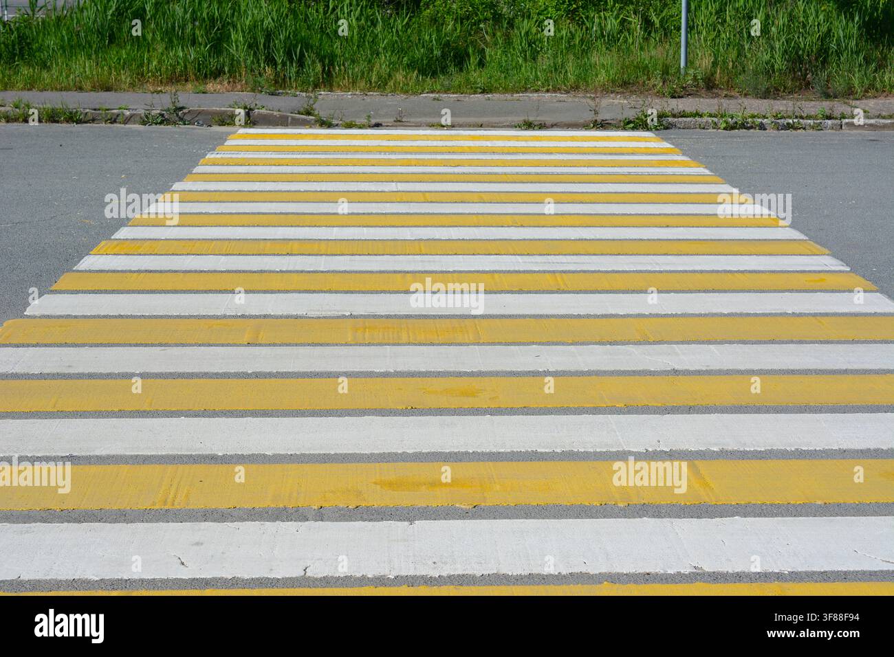 Prima piano di un passaggio pedonale a strisce gialle e bianche su una strada asfaltata Foto Stock