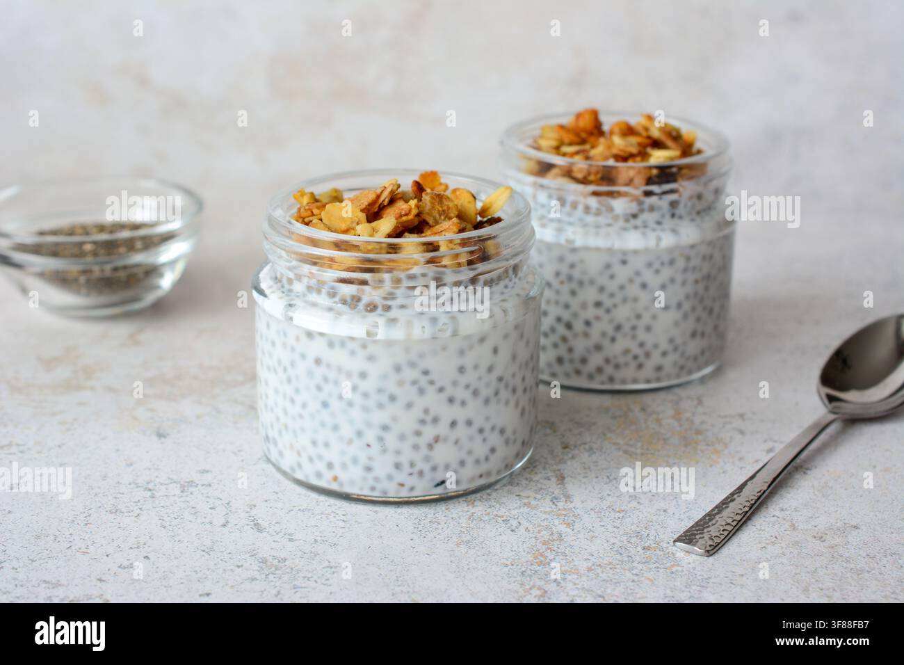 Pudding di chia con granola in barattoli di vetro e cucchiaio vista frontale Foto Stock