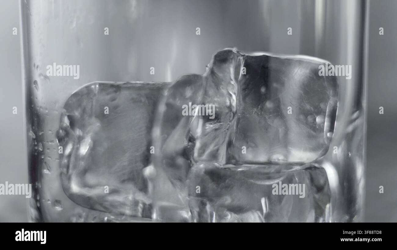 Cubetti di ghiaccio appoggiati all'interno di un bicchiere, che mostrano trasparenza e texture. La condensa aggiunge alla sensazione fredda e rinfrescante Foto Stock