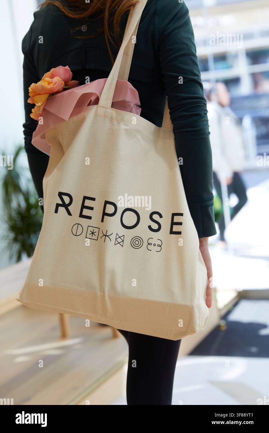 Donna che porta una borsa tote Cream Repose tenendo la borsa firmata accanto ai fiori vicino all'ingresso di Repose a Kensington, Londra, l'8 luglio 2021. Foto Stock
