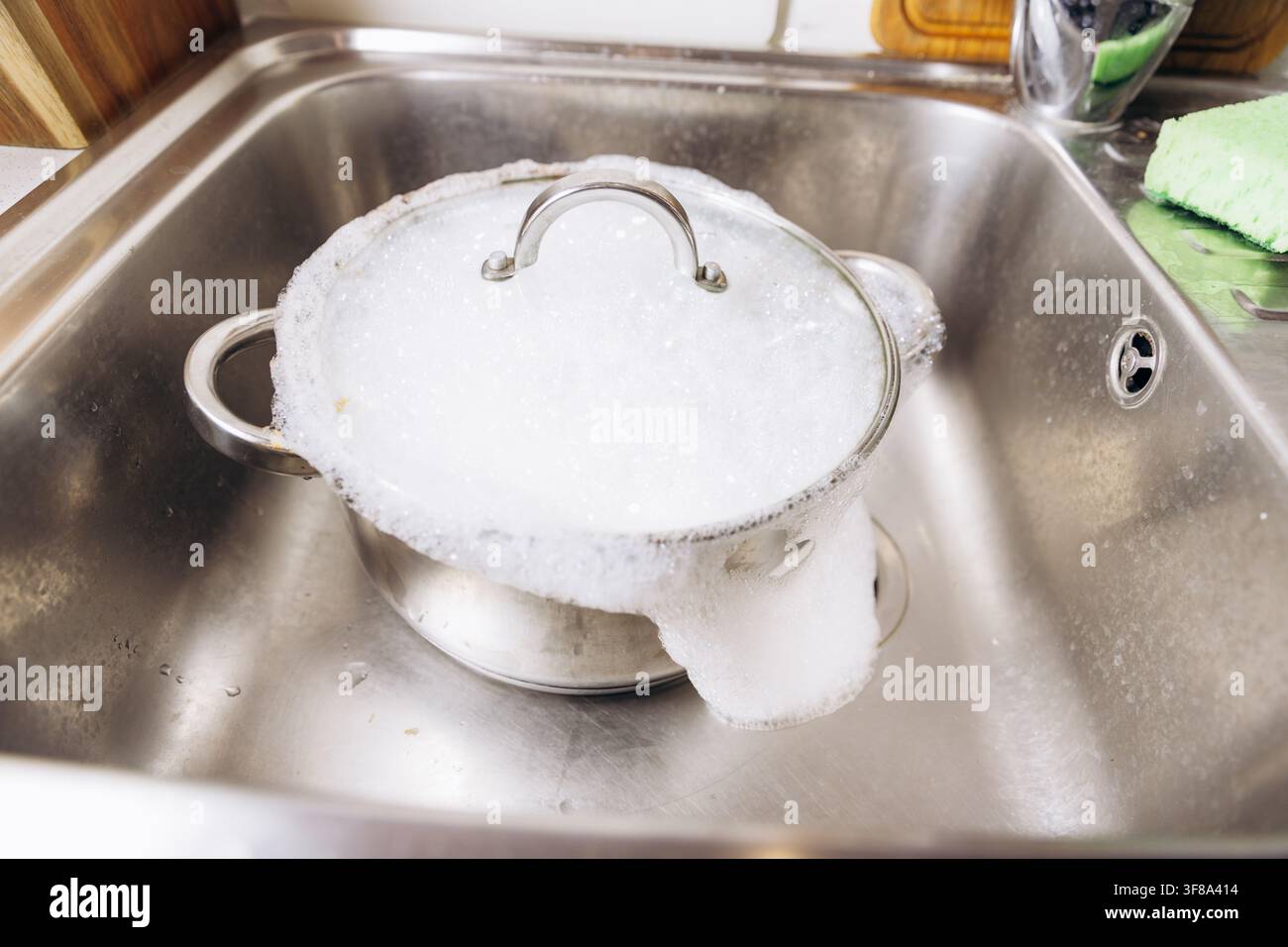 Pentola di acciaio sporca che si ammolla nel lavello della cucina con schiuma di sapone e bolle. Foto Stock