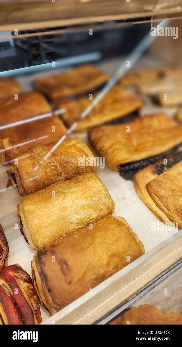 File di pain au chocolat appena sfornati mostrano una sfoglia dorata marrone chiaro e un ripieno ricco di cioccolato fondente, presentati in una vetrina di vetro in un Foto Stock