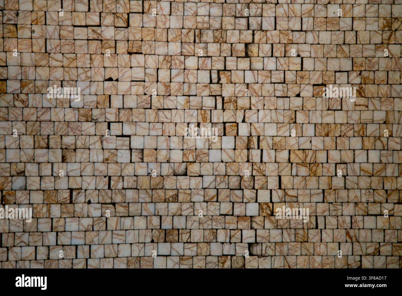 Primo piano della trama di piccole piastrelle a mosaico quadrate in marmo o pietra naturale spaccato, nei toni caldi della terra, con venature naturali visibili Foto Stock