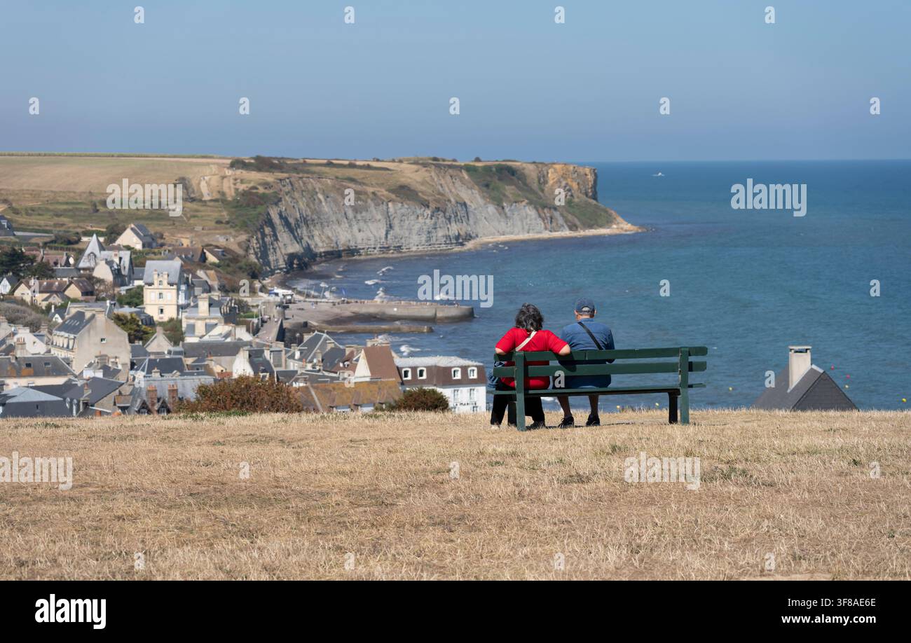 Arromanches-les-Bains, Francia - 08 11 2026: Il Giardino della Memoria. Una coppia anziana seduta su una panchina, che guarda il mare, la spiaggia, la città, cli Foto Stock