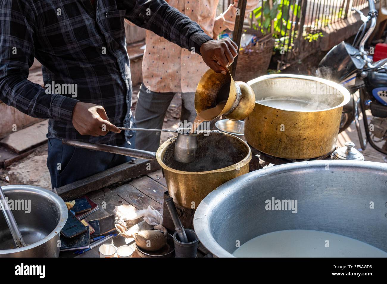 India. Rajasthan. Bundi. Preparazione del chai (tè indiano). Primo piano di un venditore ambulante che versa del chai fumante, preparato in una teiera di ottone Foto Stock