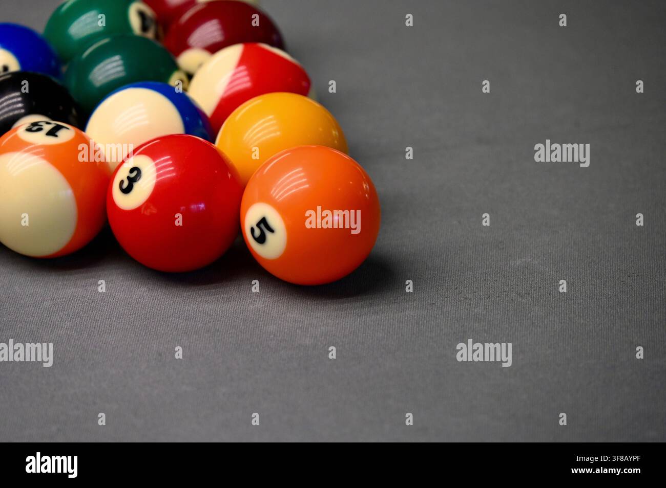Fotografia di una rastrelliera completa di palline da biliardo e pool colorate numerate disposte in una classica formazione a triangolo su uno sfondo grigio neutro. Foto Stock