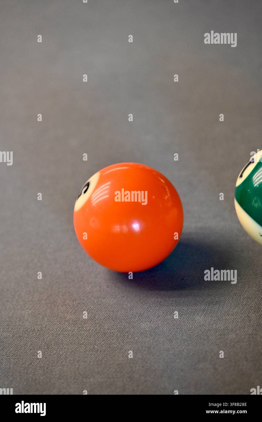 Fotografia commerciale in primo piano di una palla da biliardo arancione e di una parte di un'altra palla sul feltro grigio di un tavolo da biliardo, catturando la trama e la configurazione del gioco. Foto Stock