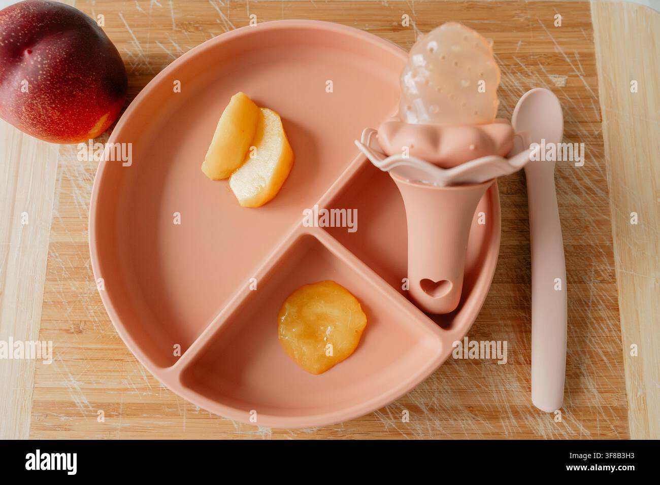 Set estetico di accessori per l'alimentazione del neonato con pappa di frutta e mordicchiatore su una superficie di legno. Foto stock perfetta per prodotti ecologici per bambini Foto Stock