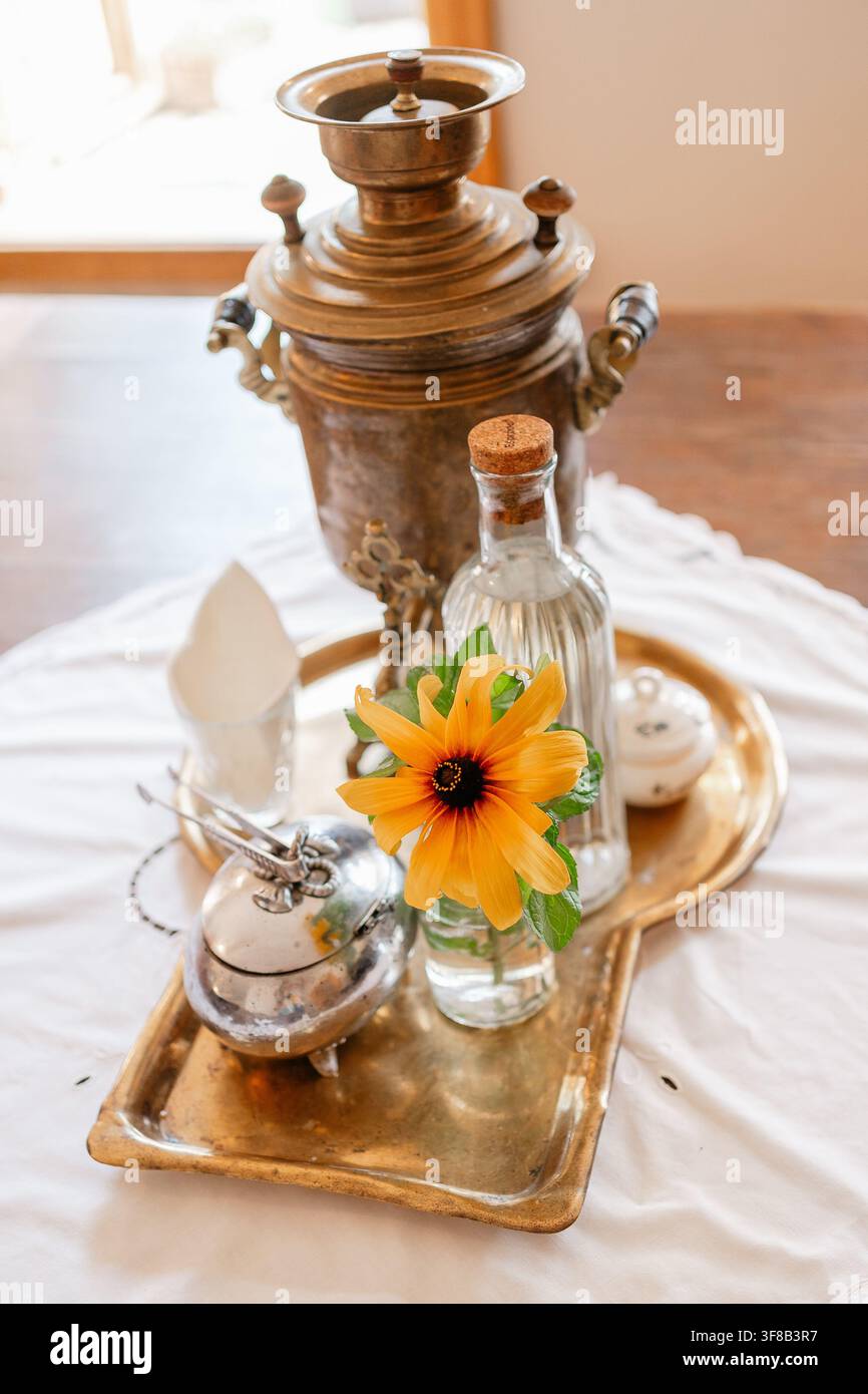 Foto ravvicinata di un samovar russo antico in ottone su un vassoio con un piccolo vaso che contiene un girasole giallo. Ideale per la tradizione della festa del tè russa, folklore Foto Stock