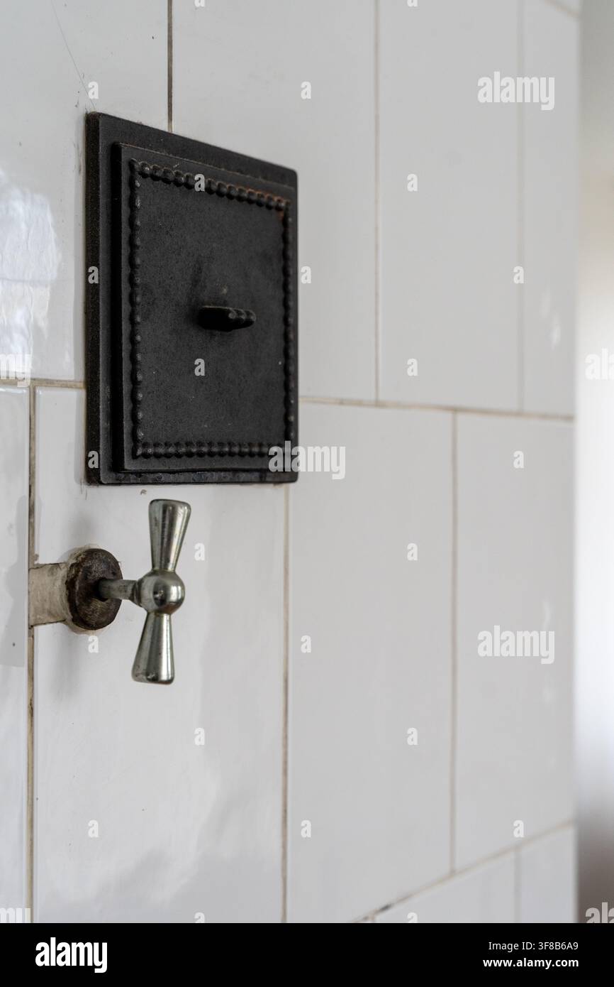 Prima di un tradizionale stufa in muratura con piastrelle bianche che mostra una porta di fuliggine in ghisa nera e una manopola del diaframma in metallo. Foto Stock